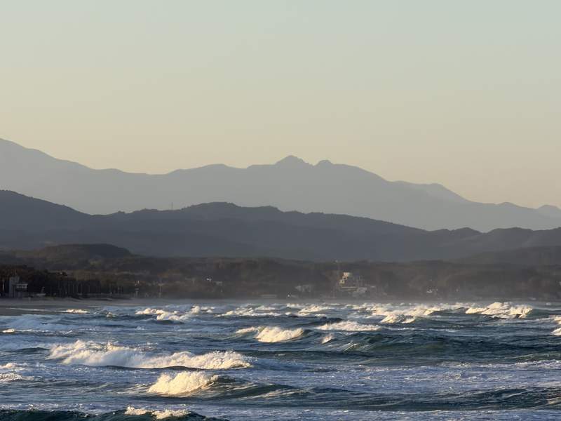 Waves rolling toward a beach with layered mountains behind