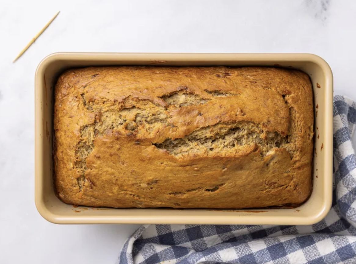 A golden baked banana bread in its pan next to a toothpick