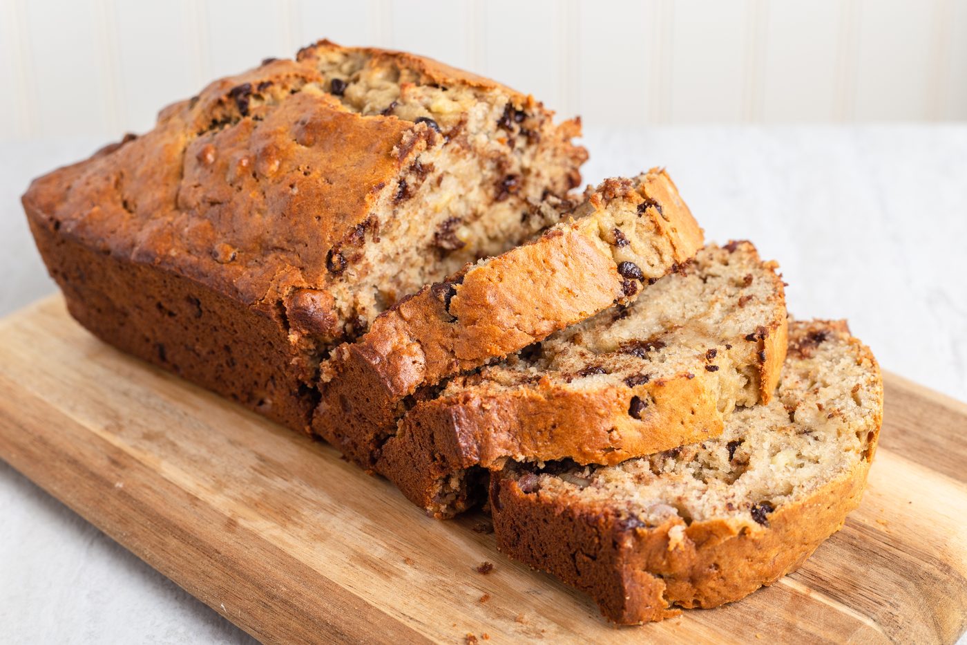 A sliced banana bread loaf on a wooden cutting board against a pale background